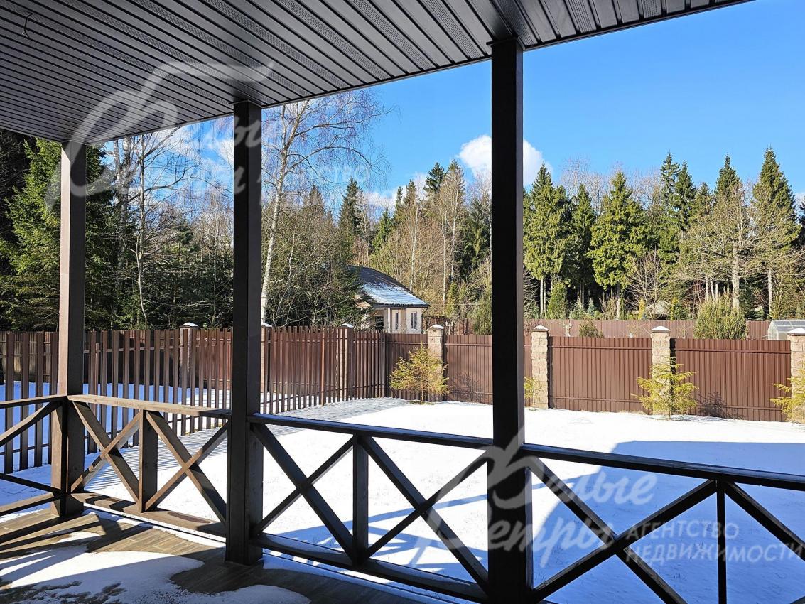 Крытая терраса с видом на участок и лес.