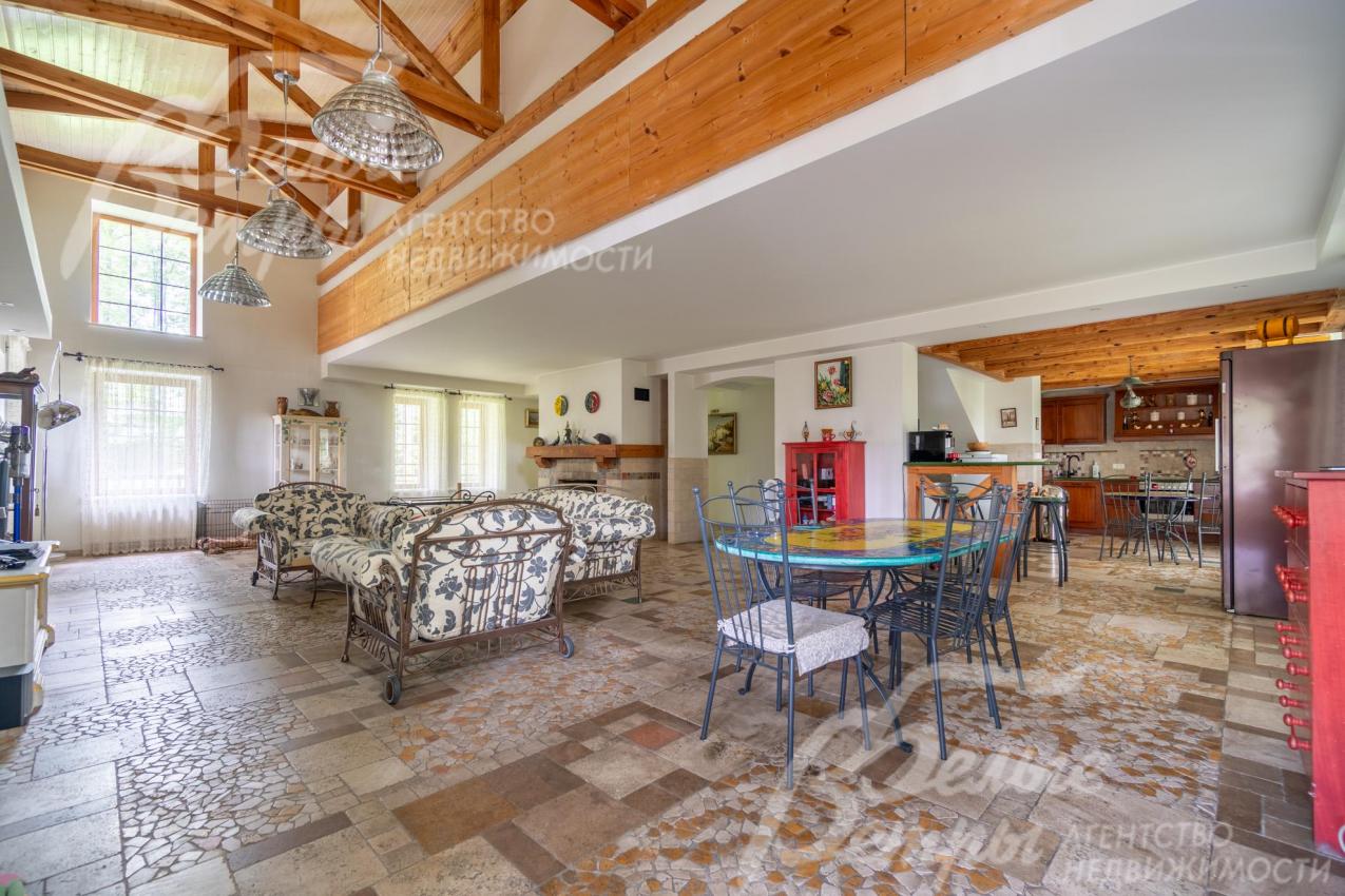 Объединённое пространство гостиной, столовой и кухни: на полу - мозаика из травертина с подогревом, на потолках из гипсокартона - массивные декоративные балки