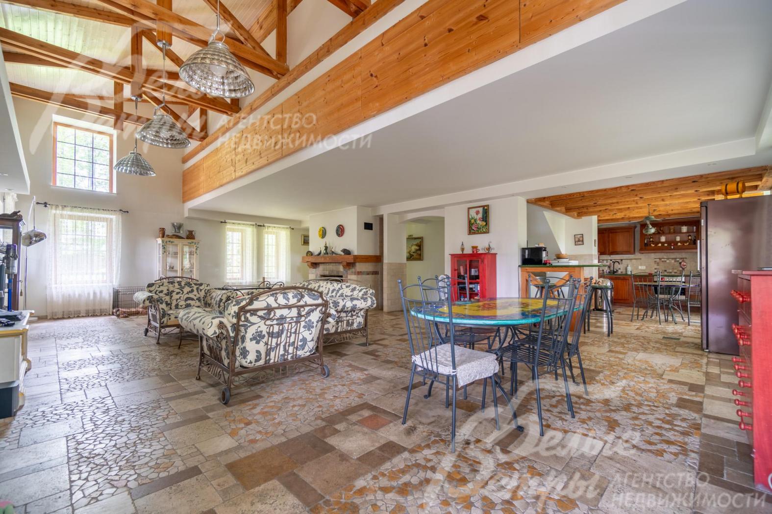 Объединённое пространство гостиной, столовой и кухни: на полу - мозаика из травертина с подогревом, на потолках из гипсокартона - массивные декоративные балки