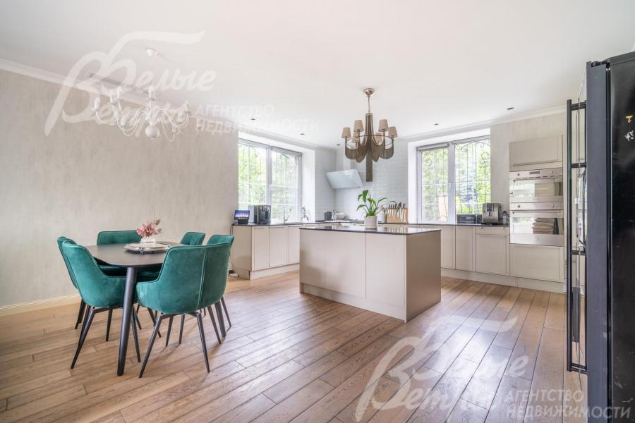 На кухне установлен светло-бежевый гарнитур из массива дерева с островом и обеденная группа