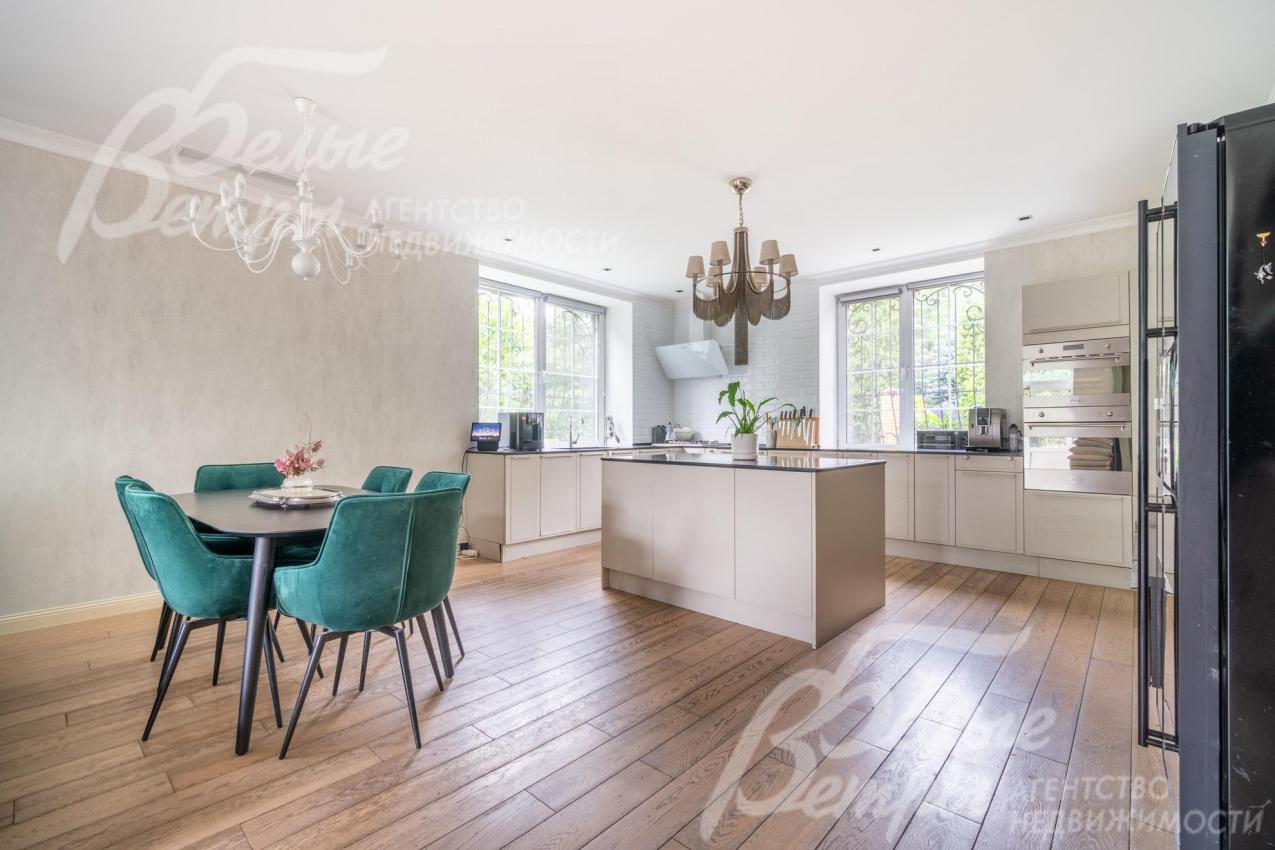 На кухне установлен светло-бежевый гарнитур из массива дерева с островом и обеденная группа