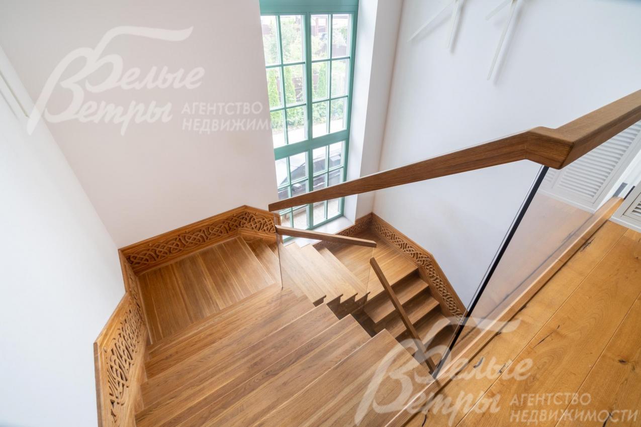 Лестница из массива дуба со стеклянным ограждением, на лестничном пролёте - высокое окно