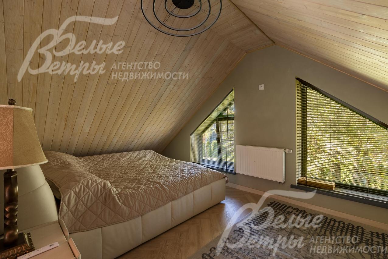 Одна из спален в гостевом доме с уютным скошенном потолком из лиственницы