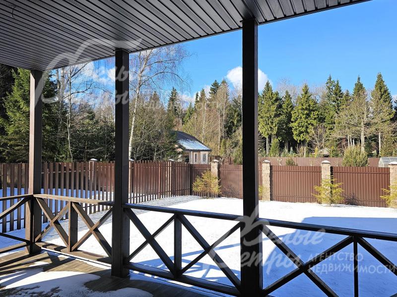 Крытая терраса с видом на участок и лес.