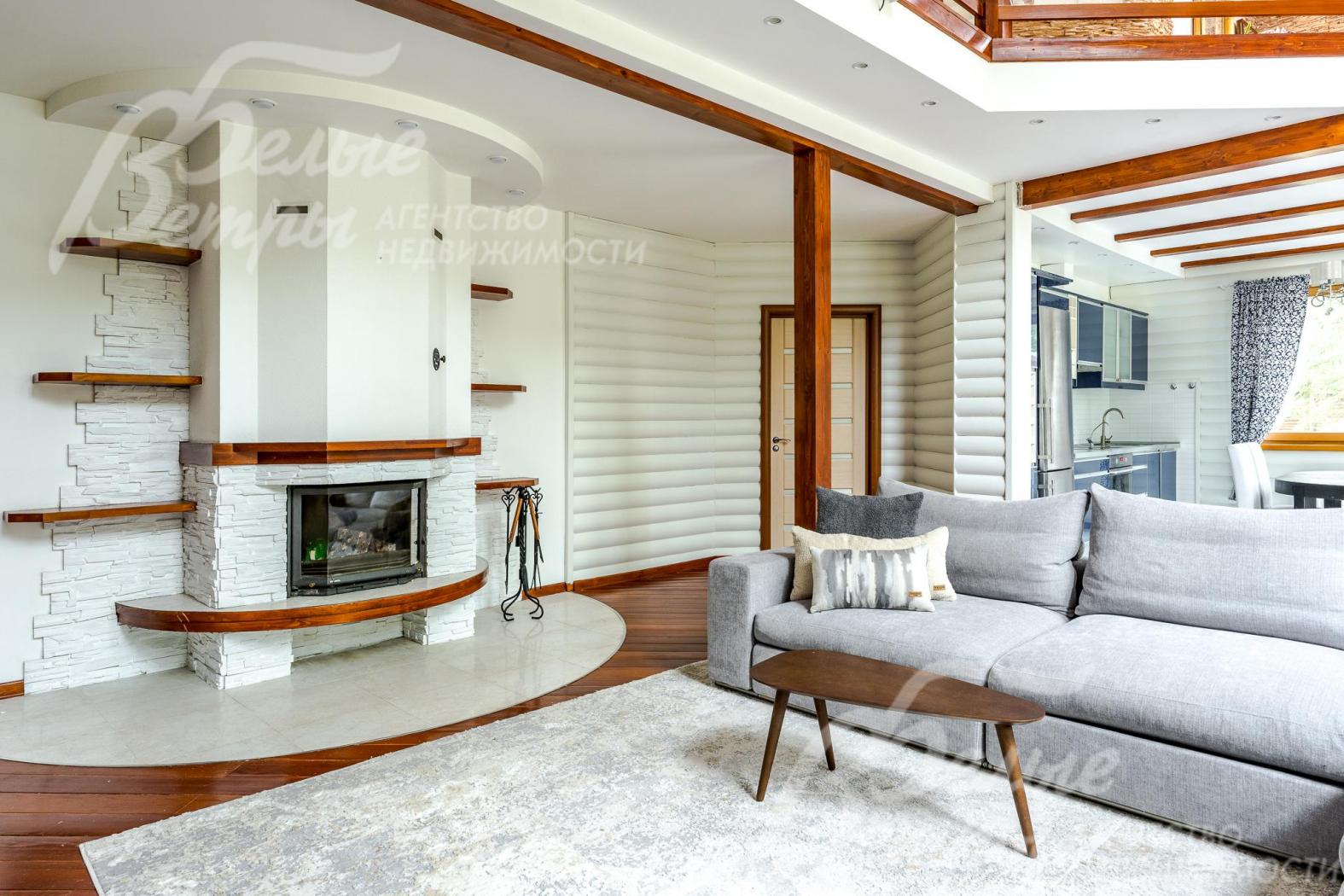 В гостиной стоит дровяной камин. Отделка стен комбинированная - покраска, блок-хаус, искусственный камень