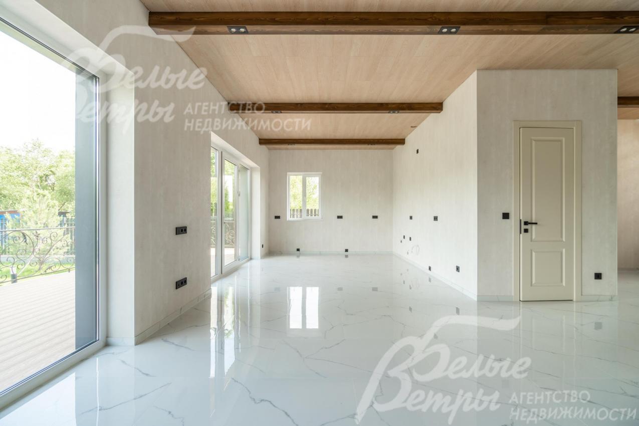 Единое пространство гостиной и кухни-столовой выглядит воздушно благодаря отделке в светлых тонах и панорамным окнам 