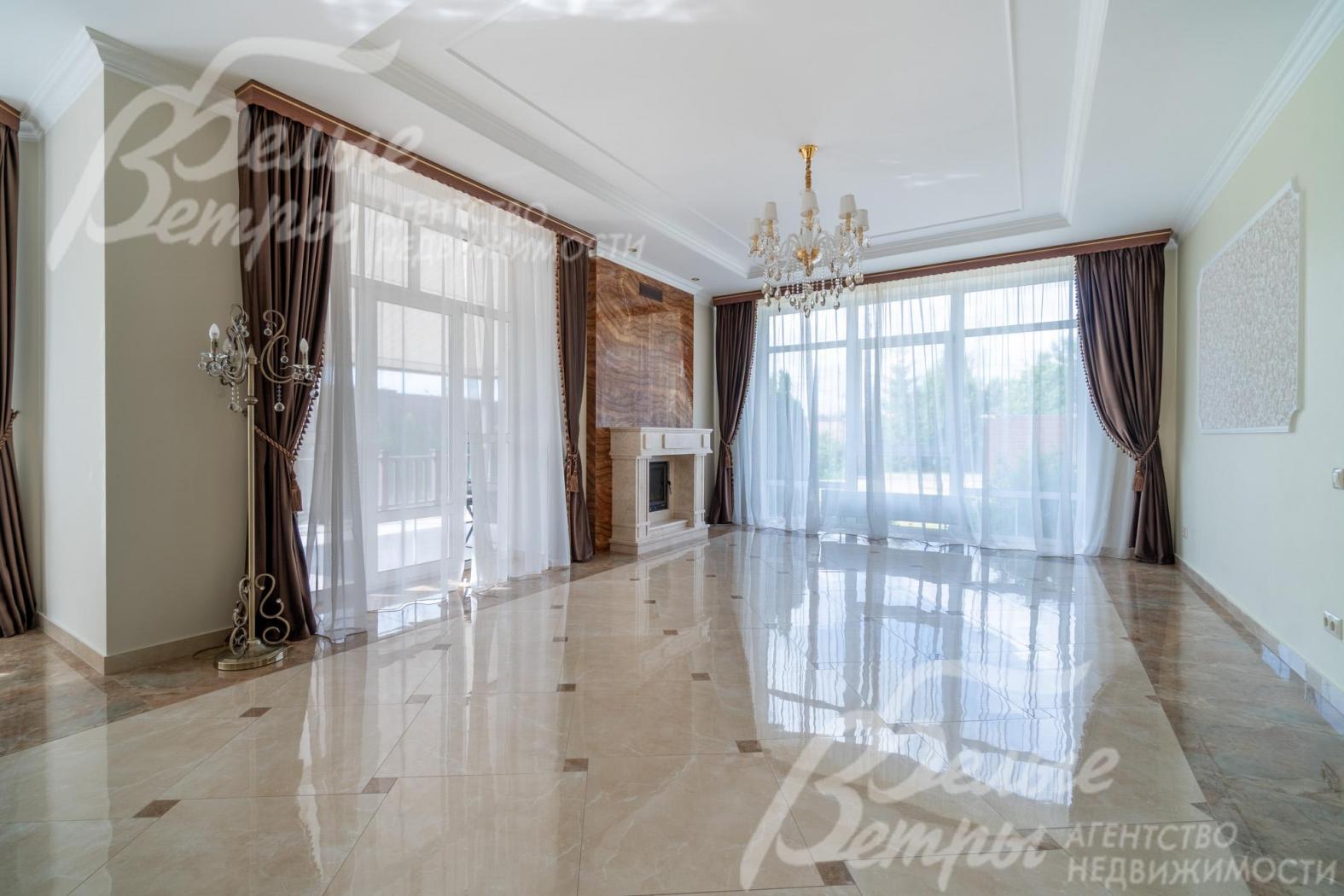 Просторная светлая гостиная с окнами в пол и выходом на крытую террасу, между окон - камин, отделанный бежевым мрамором