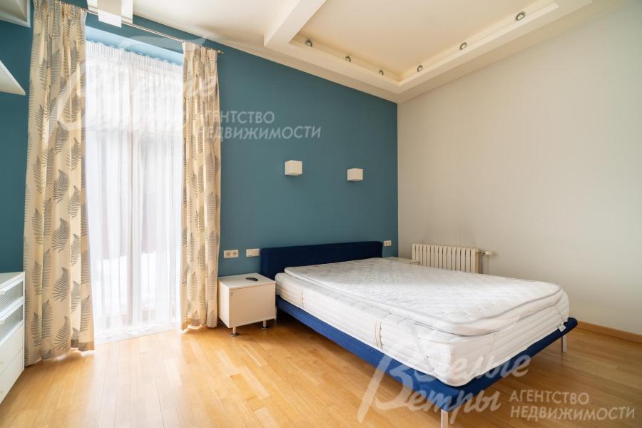 Спальня на первом этаже: акцентная стена за кроватью окрашена в спокойный тёмно-бирюзовый цвет, что добавляет глубины и создаёт уютную атмосферу