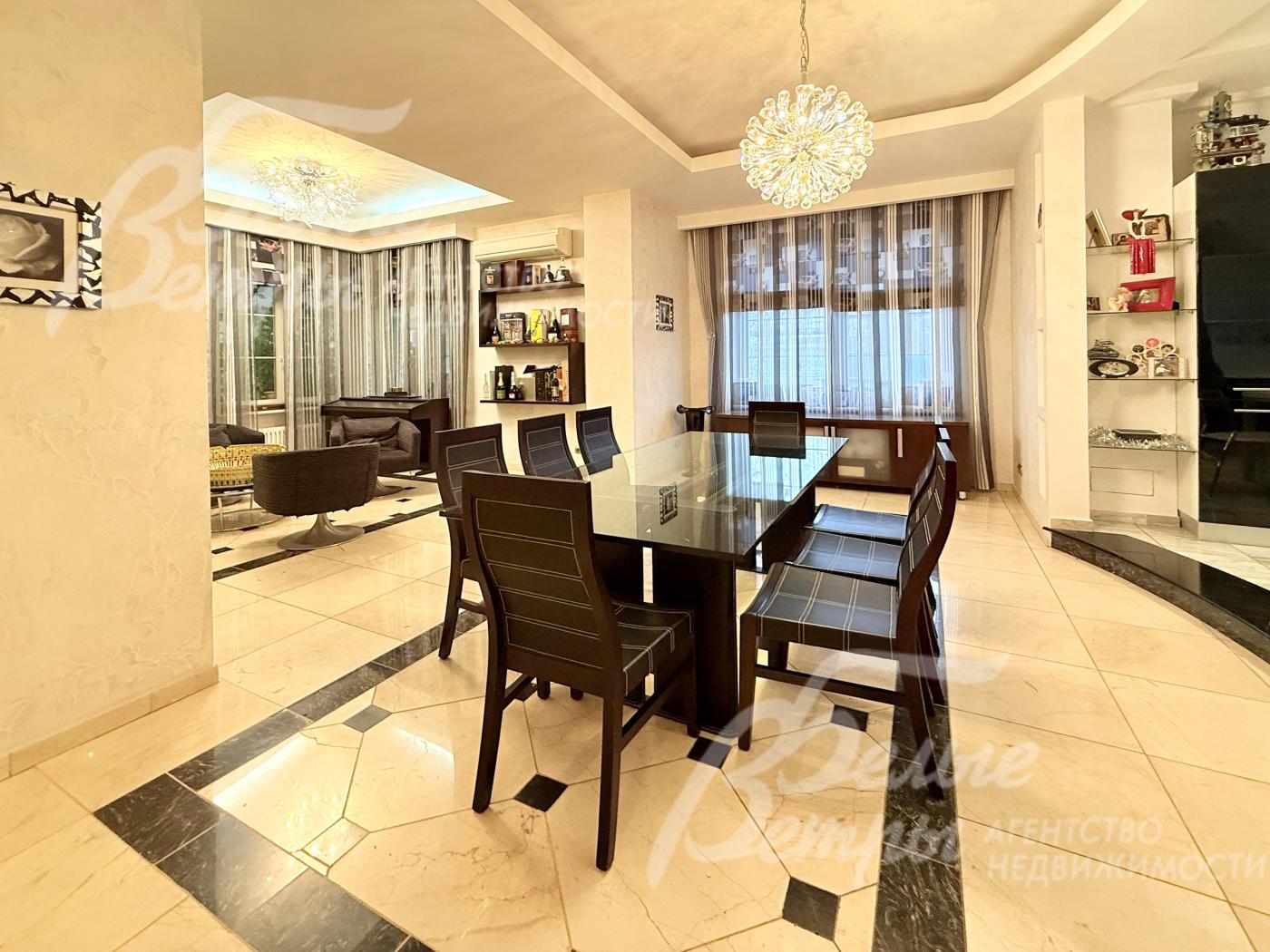 Обеденная группа со столом с тонированной стеклянной столешницей и стульями из тёмного дерева рассчитана на 8 персон