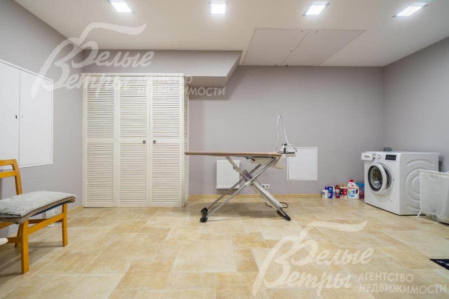 Постирочная на цокольном этаже оборудована стиральной машиной, гладильной доской и системой хранения