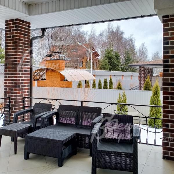 Крытая терраса с плетеной мебелью для отдыха.