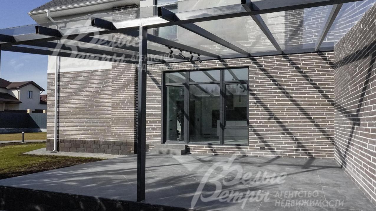 Выход на крытую террасу и участок из кухни-столовой. Оборудовано освещение участка, по периметру высажены молодые ели. 